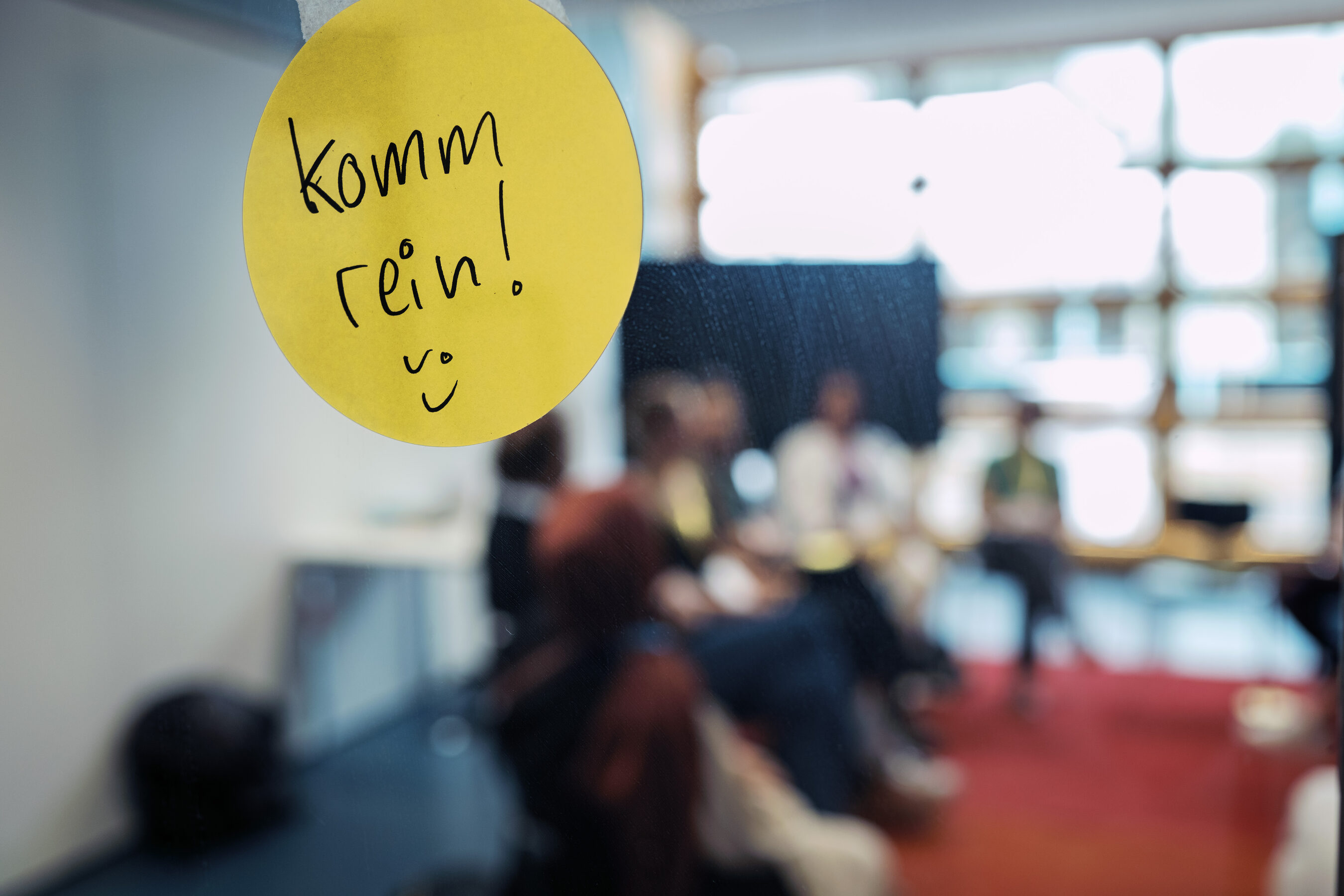 „Komm rein!“ – handgeschriebene Einladung auf gelbem Sticker, dahinter Gespräche bei einer culturediction-Konferenz