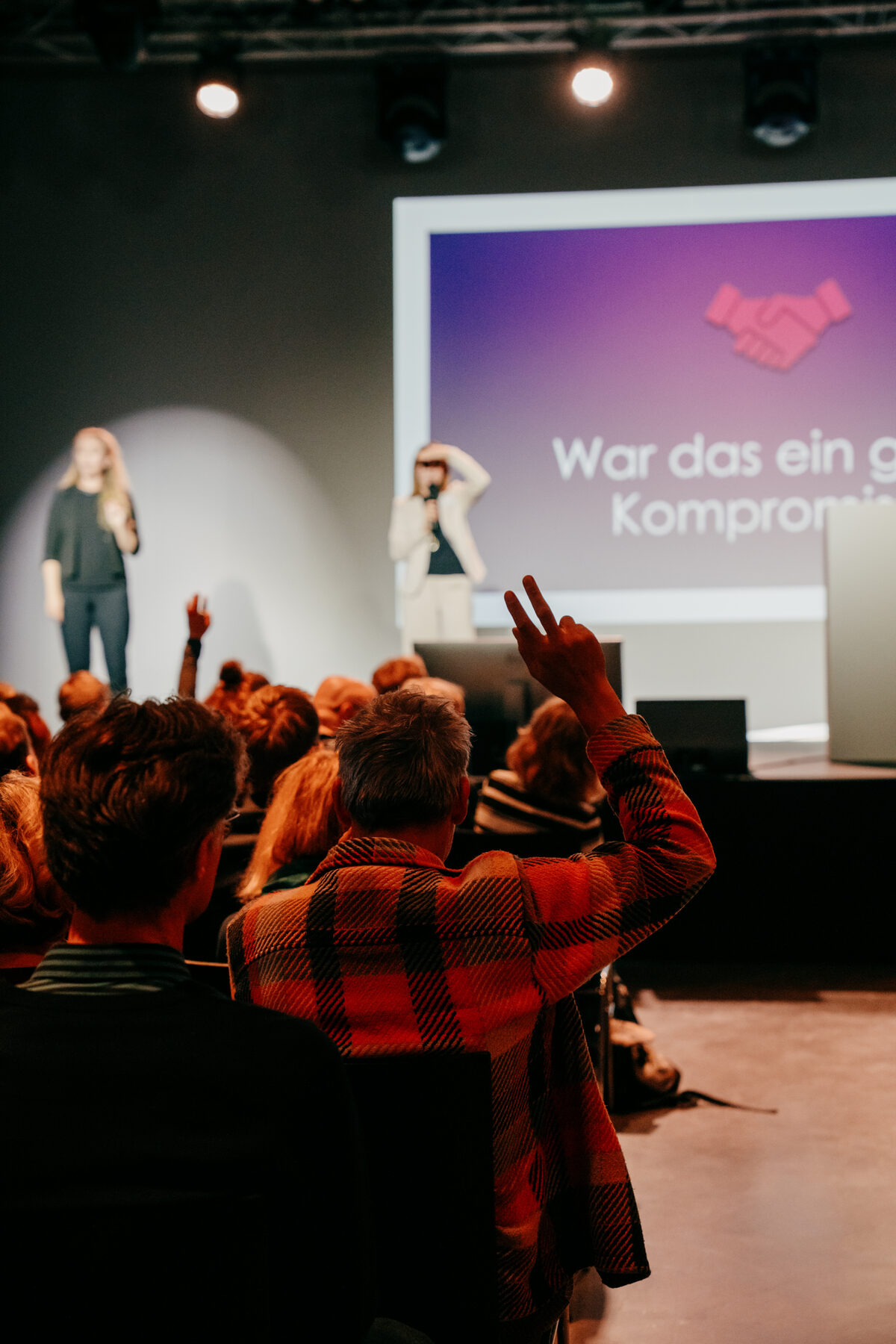 Berliner Demokratiekonferenz: Hand aus dem Publikum hebt sich für eine Frage; auf der Bühne Diskussion